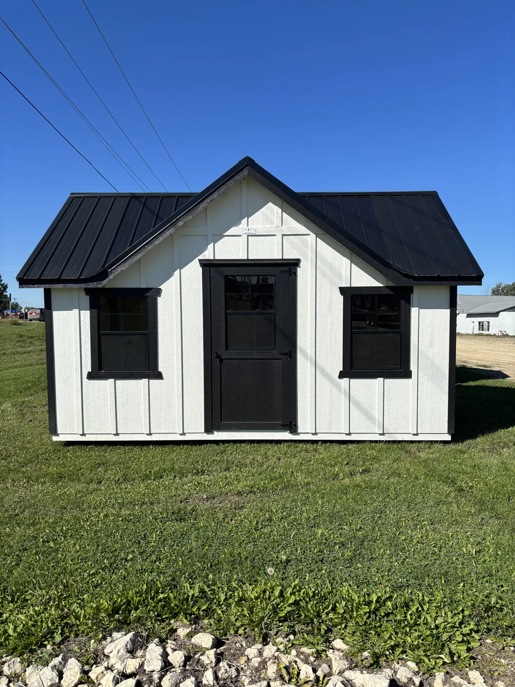 White cottage-style storage shed with black metal roof and windows at Borderland Powersports, Portage la Prairie MB